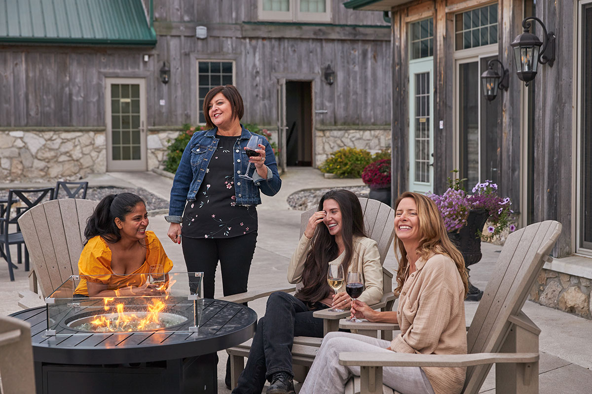 4 women smiling and laughing with fire pit and wine